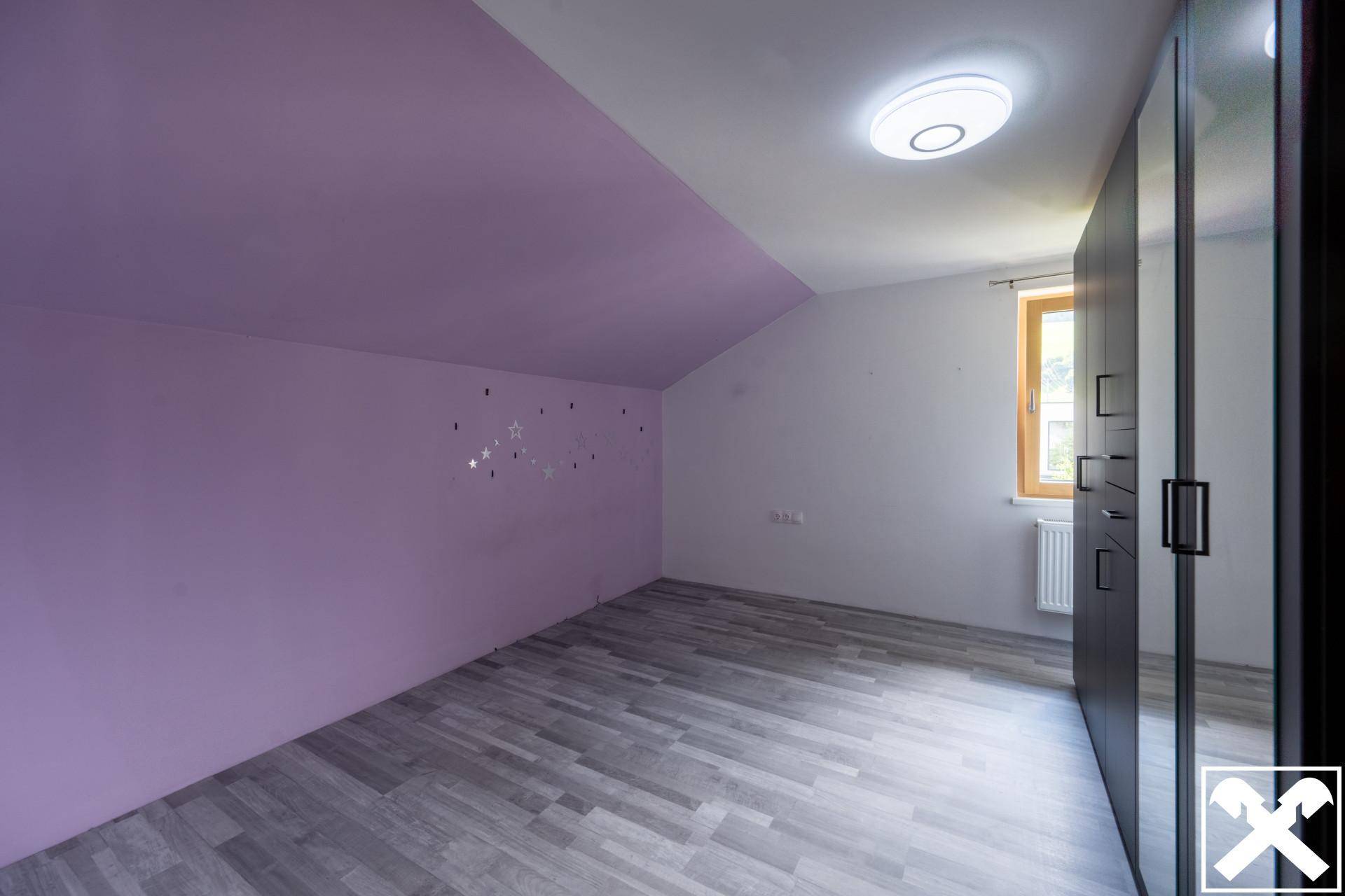 Schlafzimmer im Dachgeschoss mit lila Akzentwand, Laminatboden und Einbauschrank.