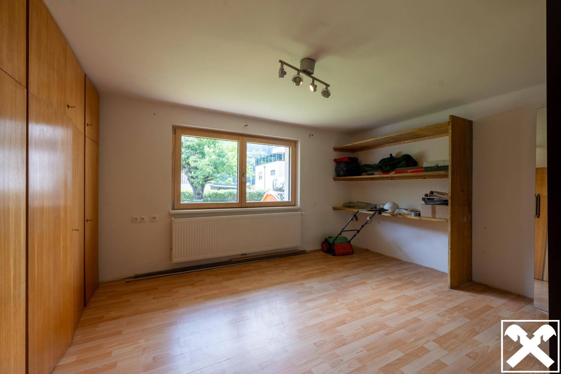 Vielseitiger Raum mit Holzschränken, Regalen und Fenster, ideal als Abstellraum oder Büro.