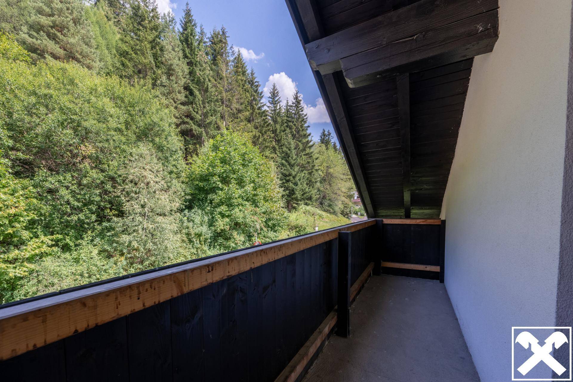 Überdachter Balkon mit Holzboden und Blick auf die bewaldeten Berghänge.