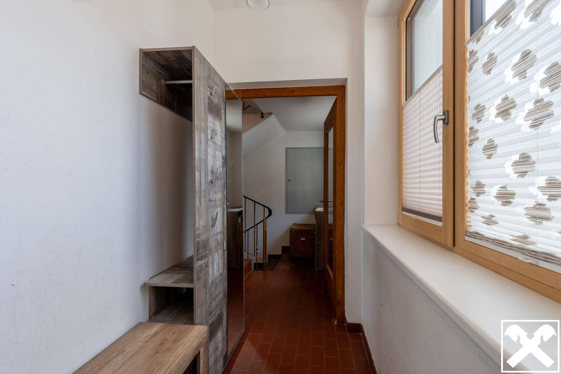 Eingangsbereich mit Fliesenboden, Garderobe und Fenster, das Tageslicht hereinlässt.