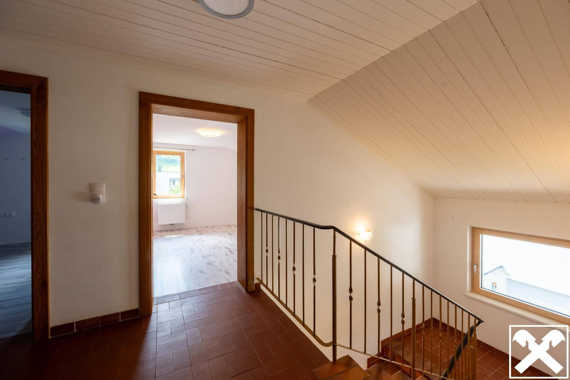 Treppenhaus mit Fliesenboden, schmiedeeisernem Geländer und Holzdecke.