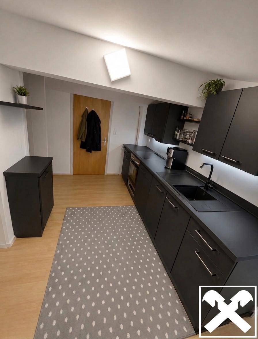 Moderne Küche mit schwarzen Schränken, heller Laminatboden und schräger Decke.