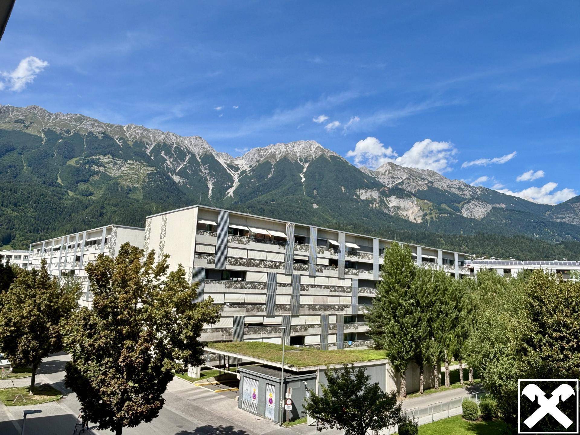 Mehrfamilienhaus mit moderner Architektur und beeindruckendem Alpenpanorama im Hintergrund.