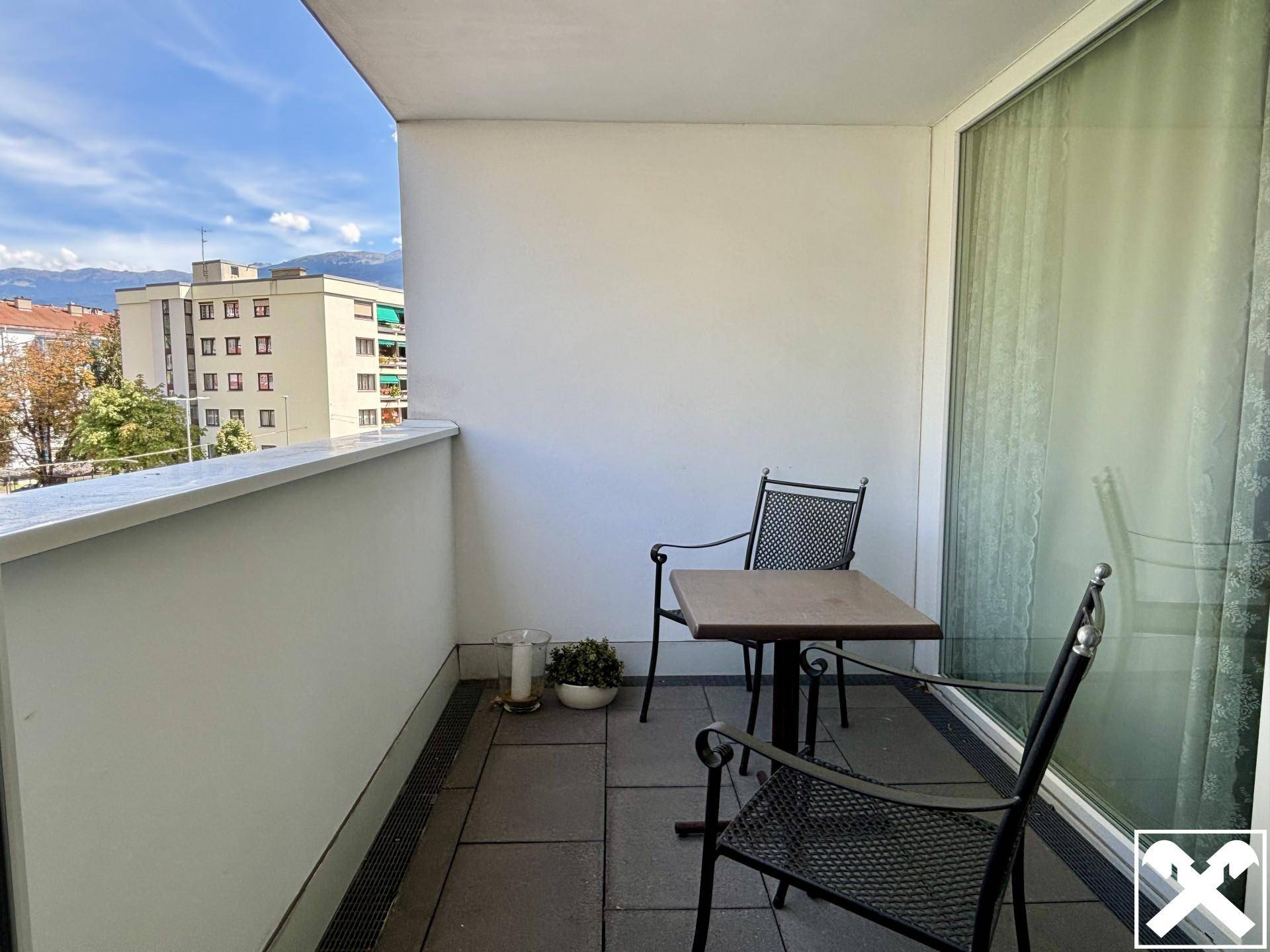 Kleiner Balkon mit Sitzgelegenheiten und Blick auf die umliegenden Gebäude und Berge.
