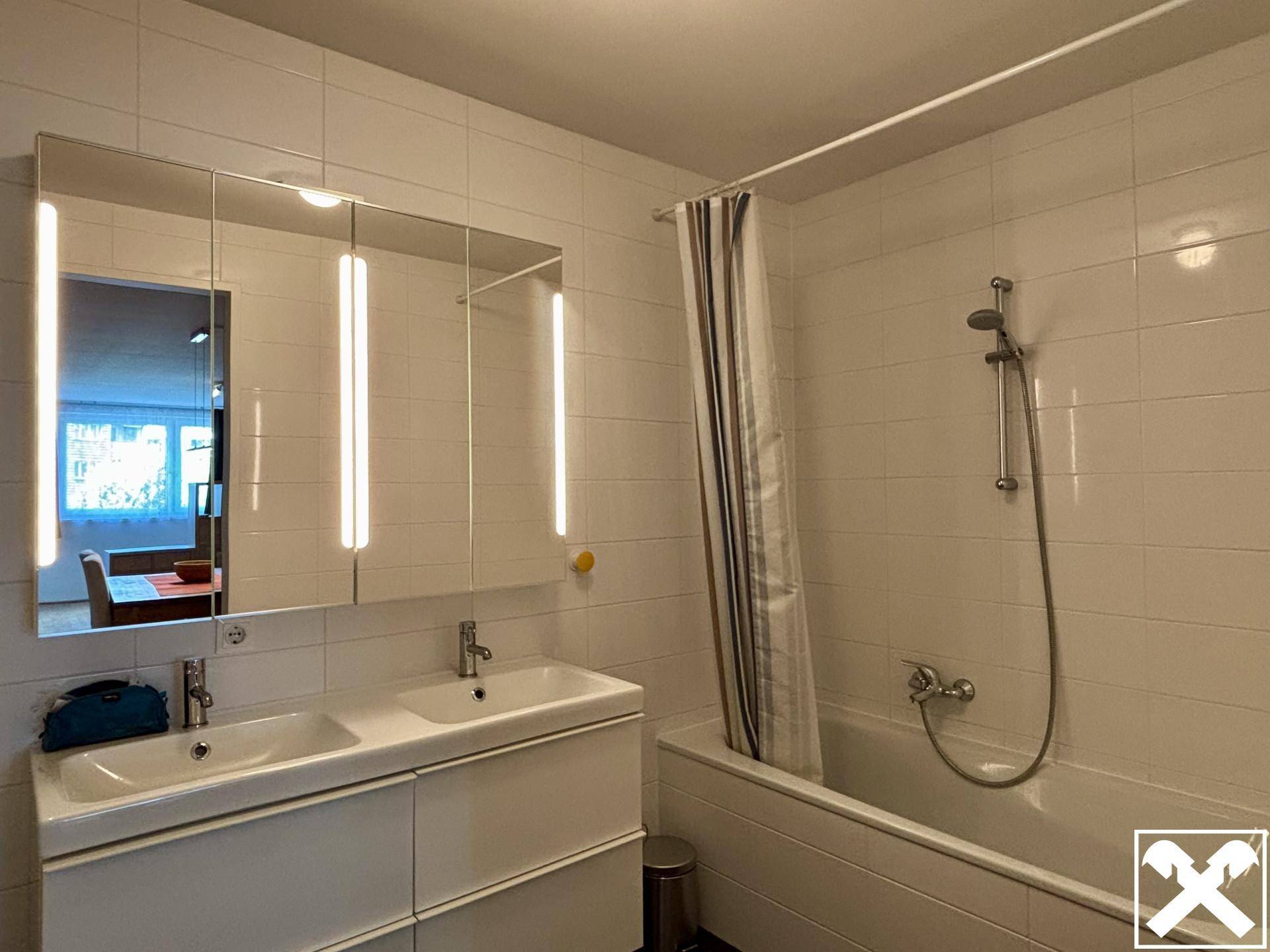 Modernes Badezimmer mit Badewanne, Duschfunktion und Doppelwaschbecken, hell gefliest.