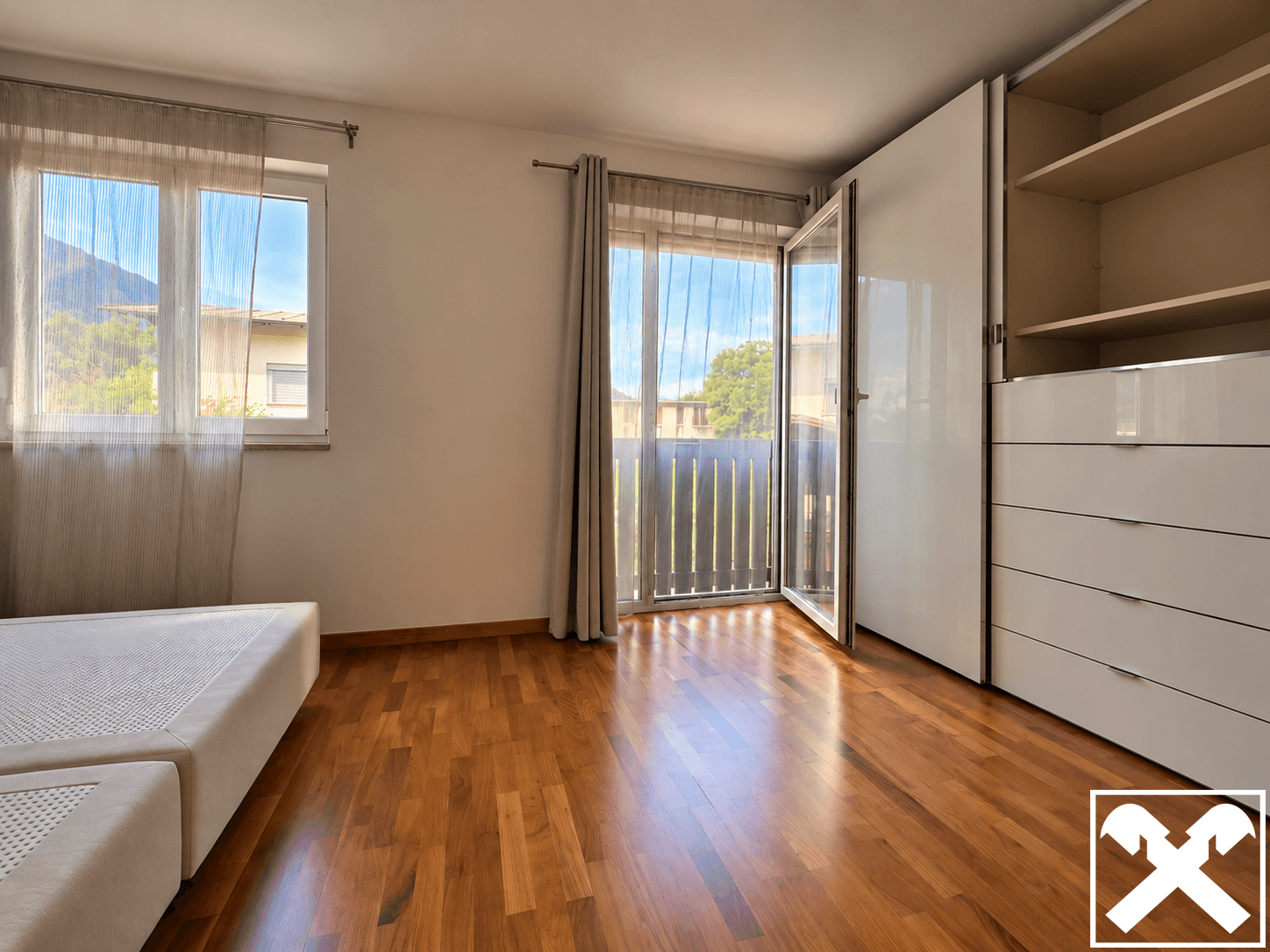Helles Schlafzimmer mit Holzboden, Einbauschrank und Zugang zu einem französischen Balkon.