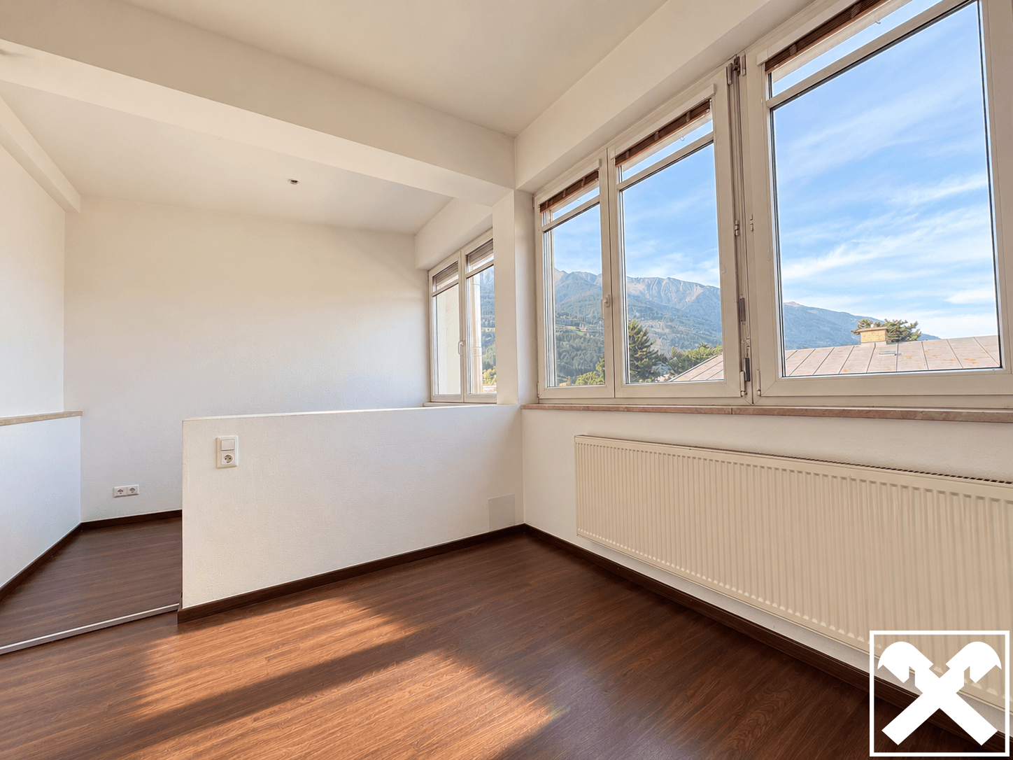 Lichtdurchfluteter Raum mit Laminatboden und Panoramablick auf die Berge und grüne Umgebung.