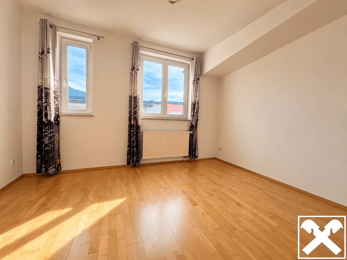 Geräumiges Zimmer mit hellem Holzboden, großen Fenstern und viel Tageslicht.