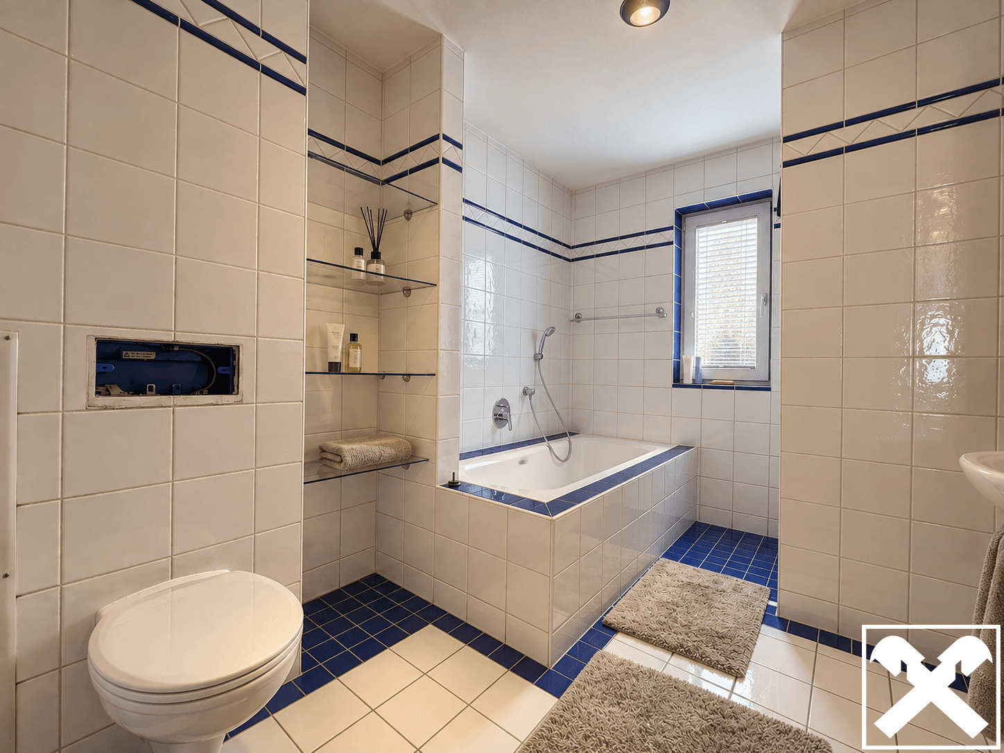 Badezimmer mit blauen Akzentfliesen, Badewanne und integriertem WC.