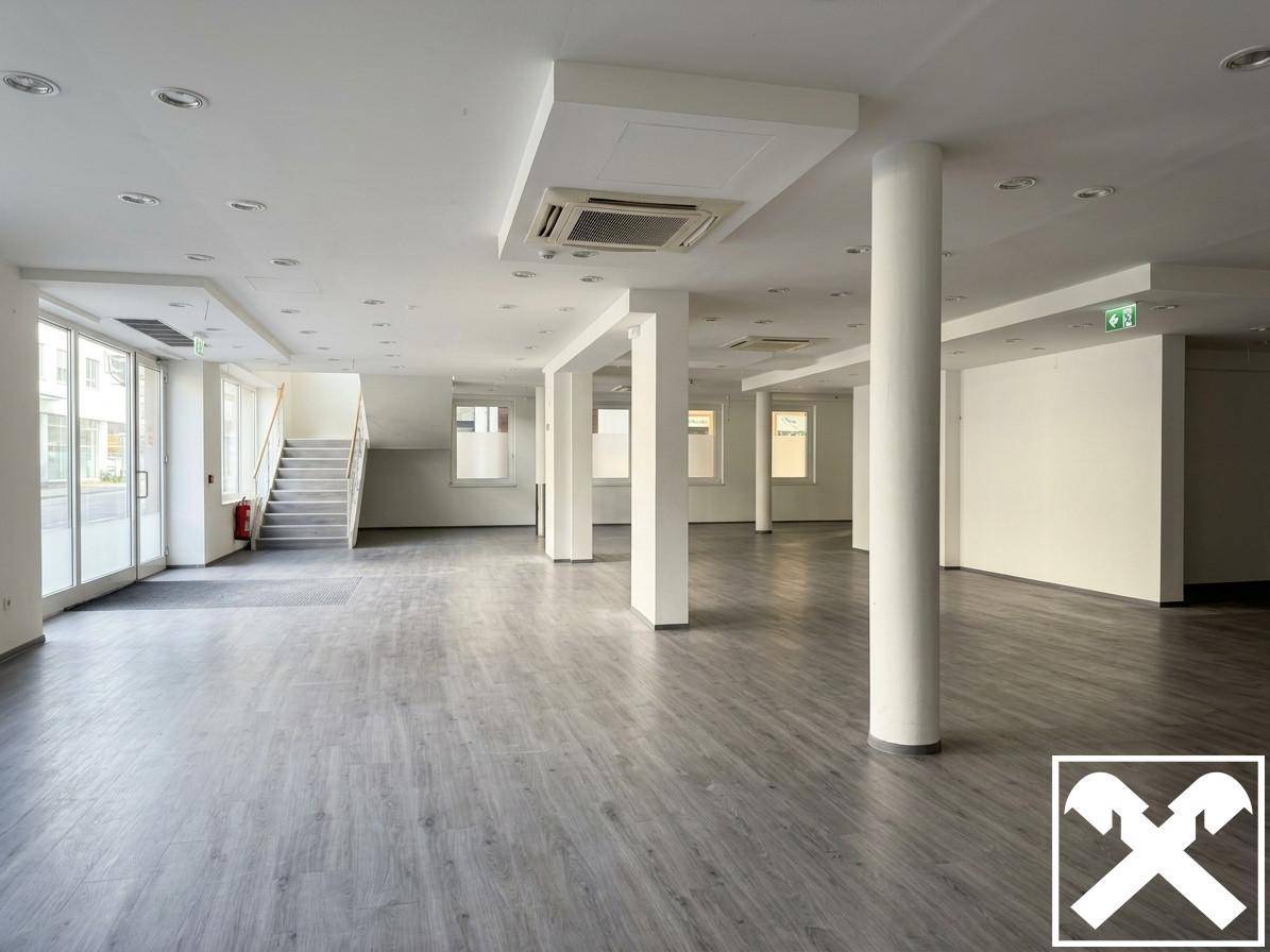 Heller Gewerberaum mit großen Fenstern, grauen Plankenböden und einer Treppe zum oberen Bereich.