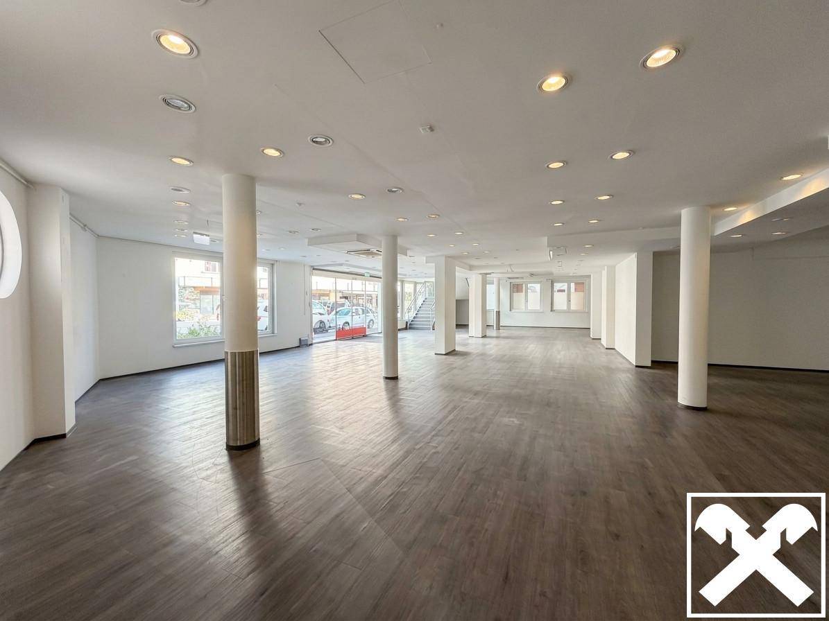 Weitläufiger Verkaufsraum mit dunklem Plankenboden, vielen Säulen und großen Schaufenstern zur Straße.