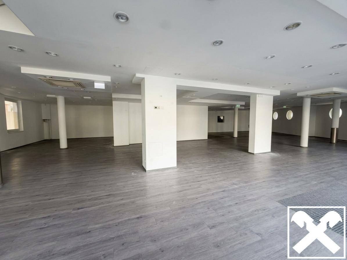 Großer, offener Gewerberaum mit zahlreichen weißen Säulen, abgehängter Decke und modernem Bodenbelag.