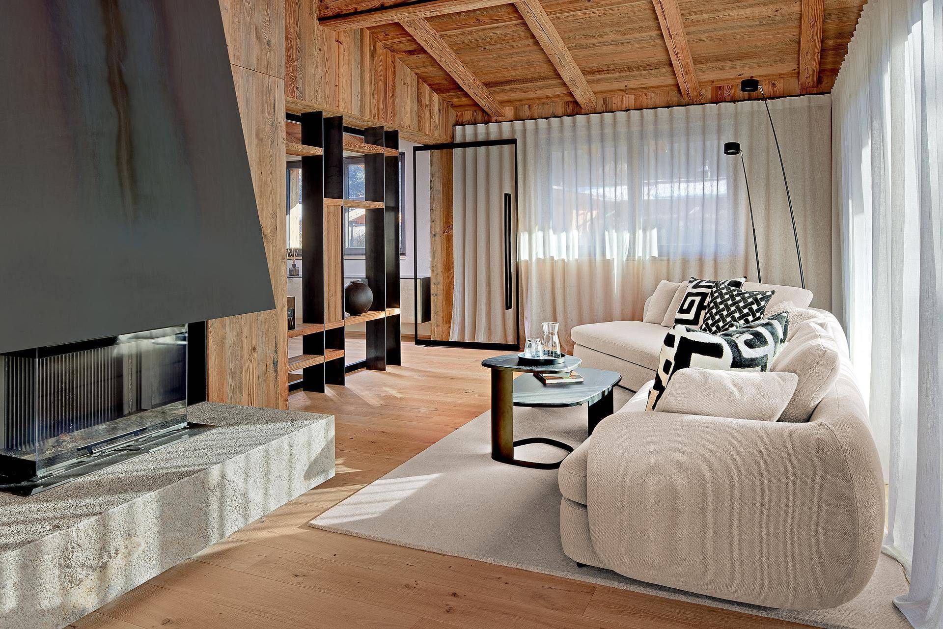 Gemütliches Wohnzimmer mit Holzbalkendecke, modernem Kamin und bequemer Couch.