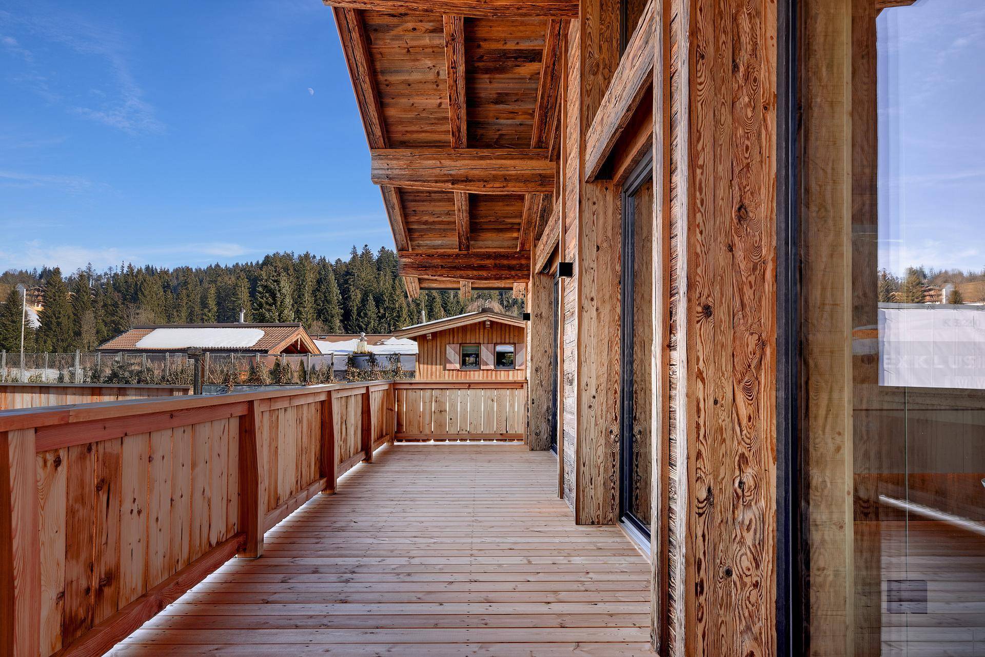 Geräumiger Holzbalkon mit Blick auf die umliegende Berglandschaft und die verschneiten Dächer.