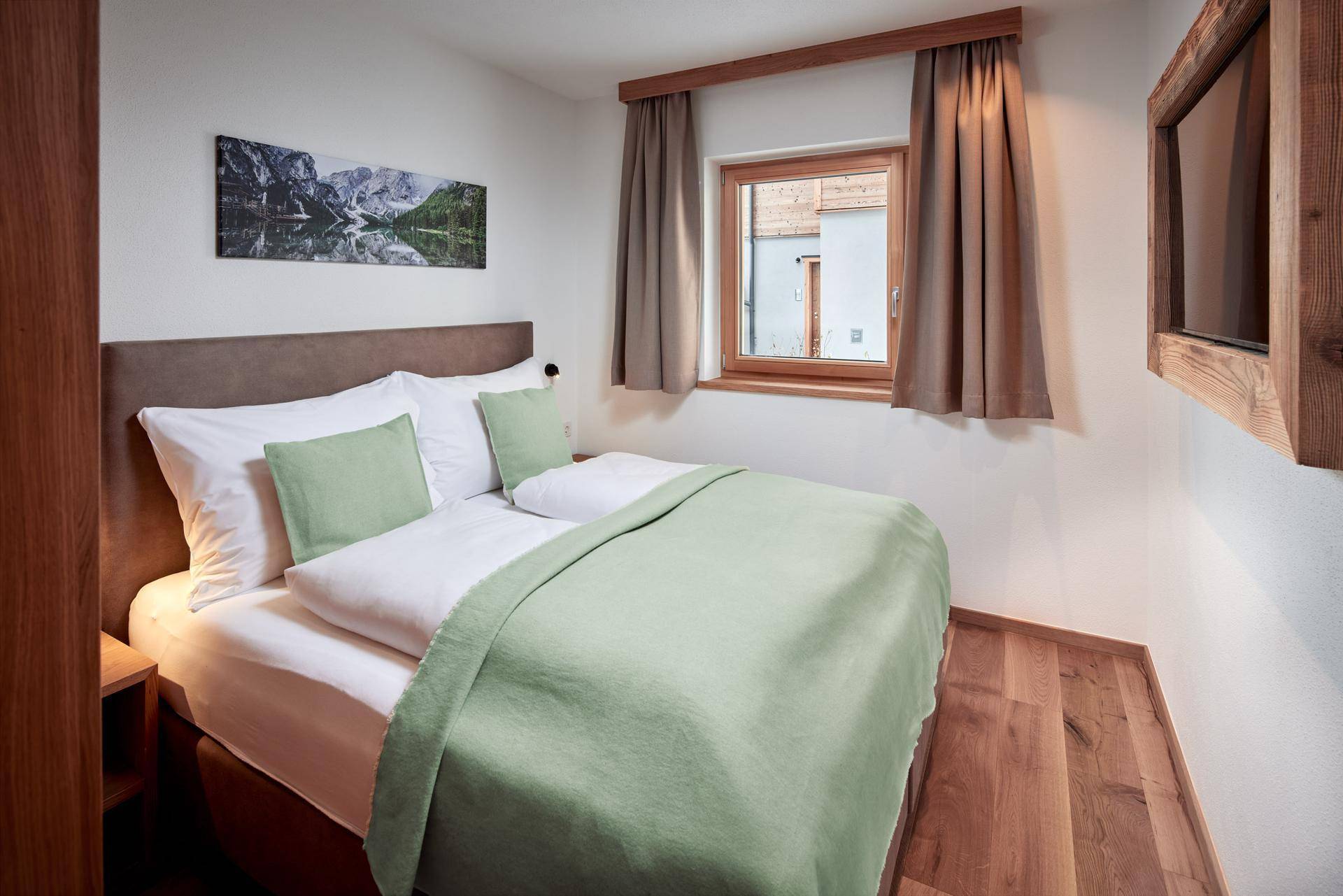 Helles Schlafzimmer mit Doppelbett, Holzboden und Blick auf die umliegenden Gebäude.