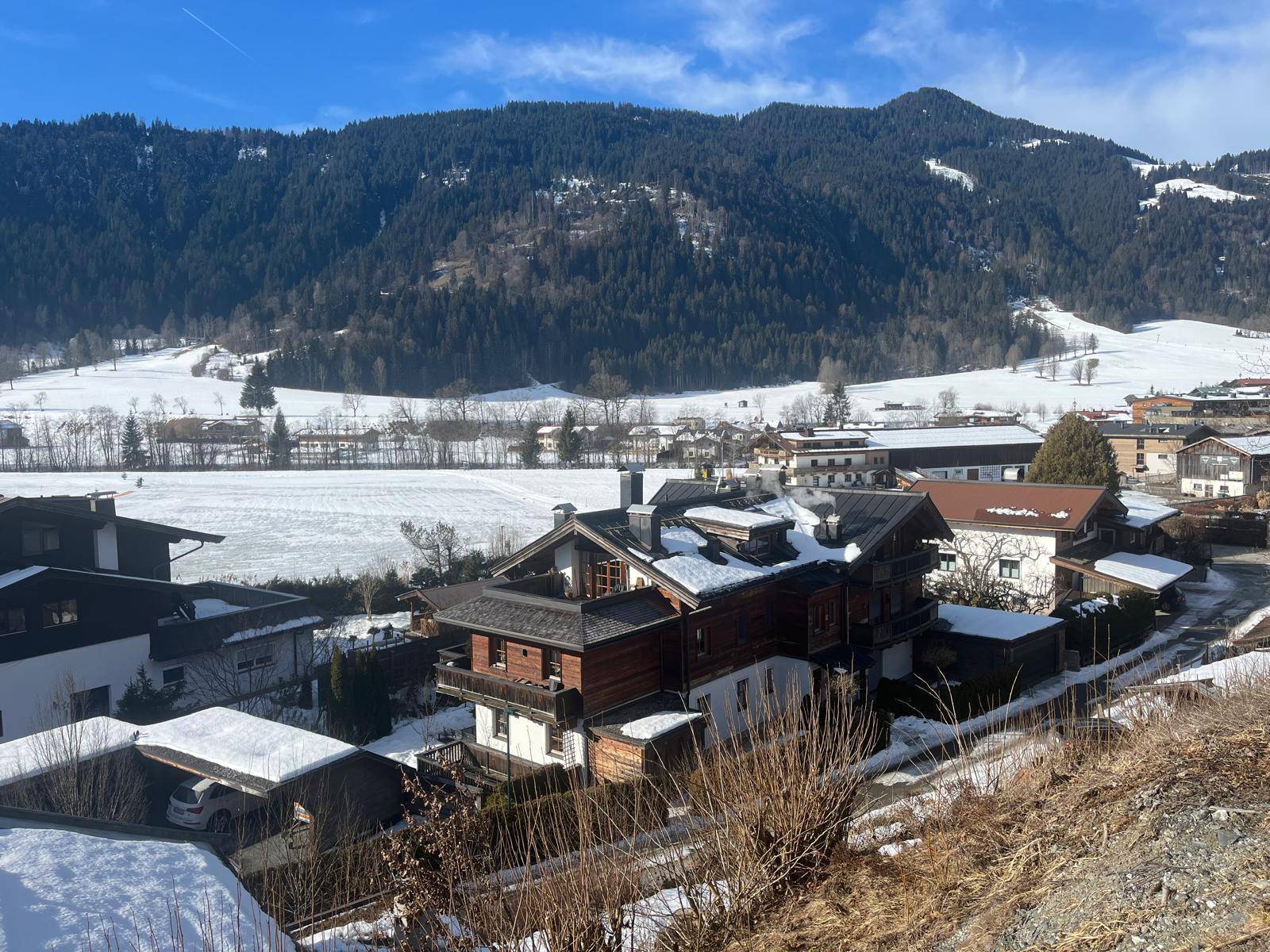 Winterlicher Ausblick auf ein Wohngebiet mit traditionellen Häusern und schneebedeckten Bergen.