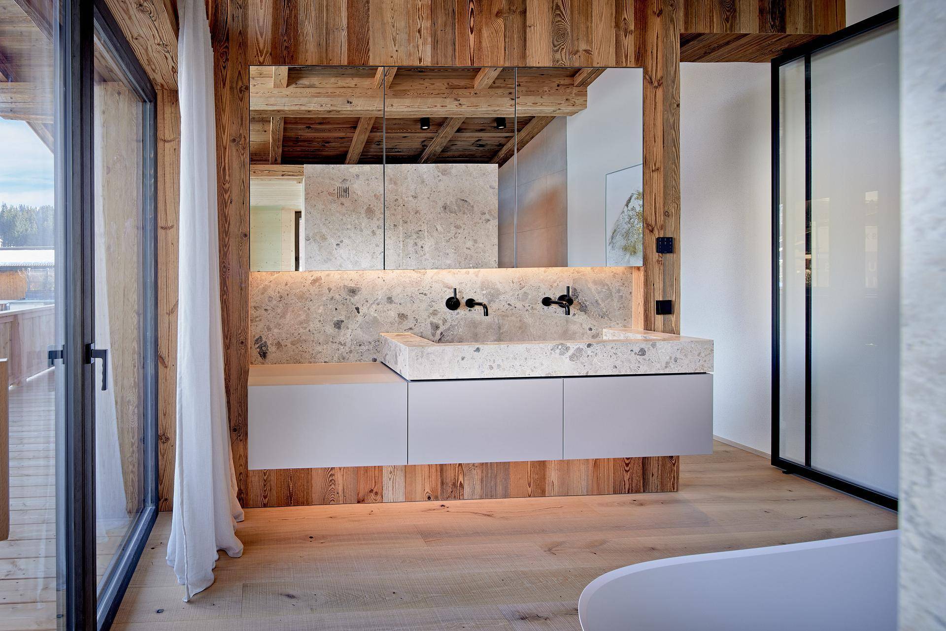 Modernes Badezimmer mit Doppelwaschbecken aus Stein, großem Spiegel und Holzwänden.