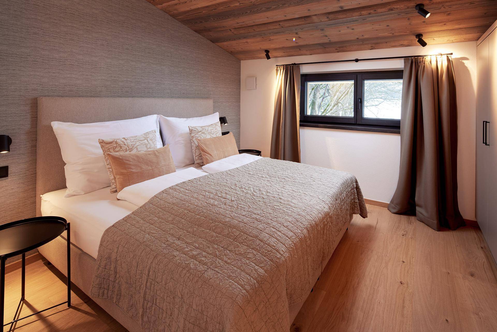 Helles Schlafzimmer mit Holzbalkendecke, Doppelbett und Blick auf die verschneite Landschaft.