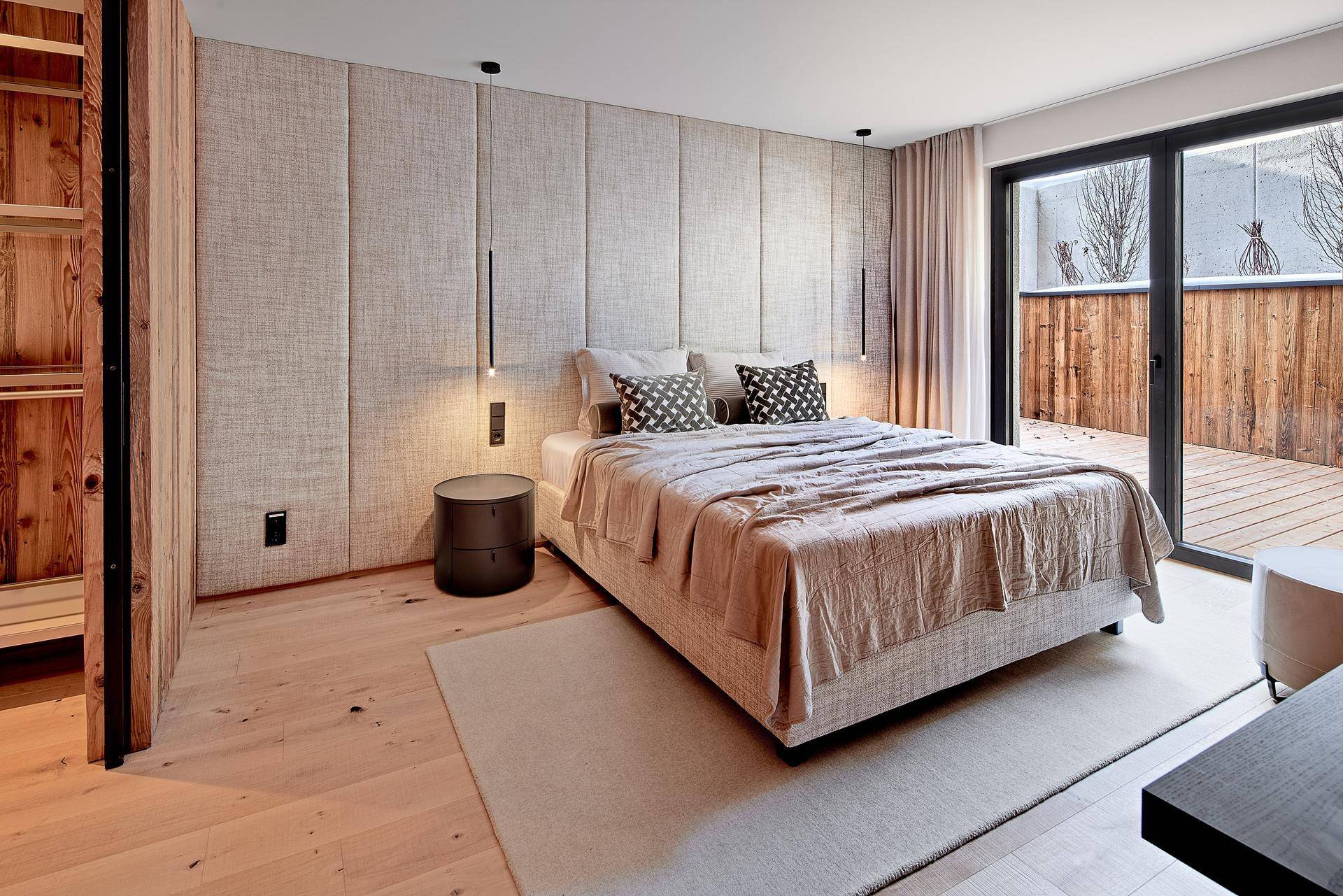 Modernes Schlafzimmer mit Holzboden, gepolsterter Wand und Zugang zu einem Außenbereich.