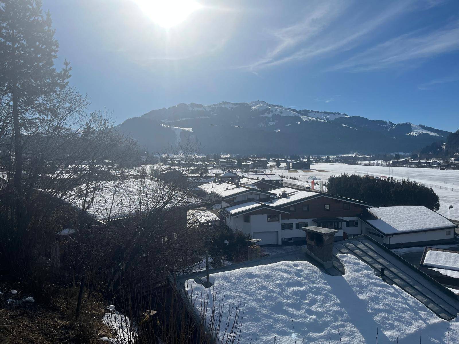 Sonniger Blick über eine verschneite Wohngegend mit Bergen im Hintergrund unter blauem Himmel.