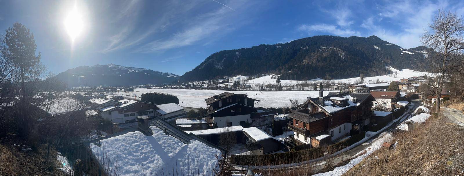 Weitläufiger Panoramablick über eine verschneite alpine Landschaft mit Häusern und Bergen.