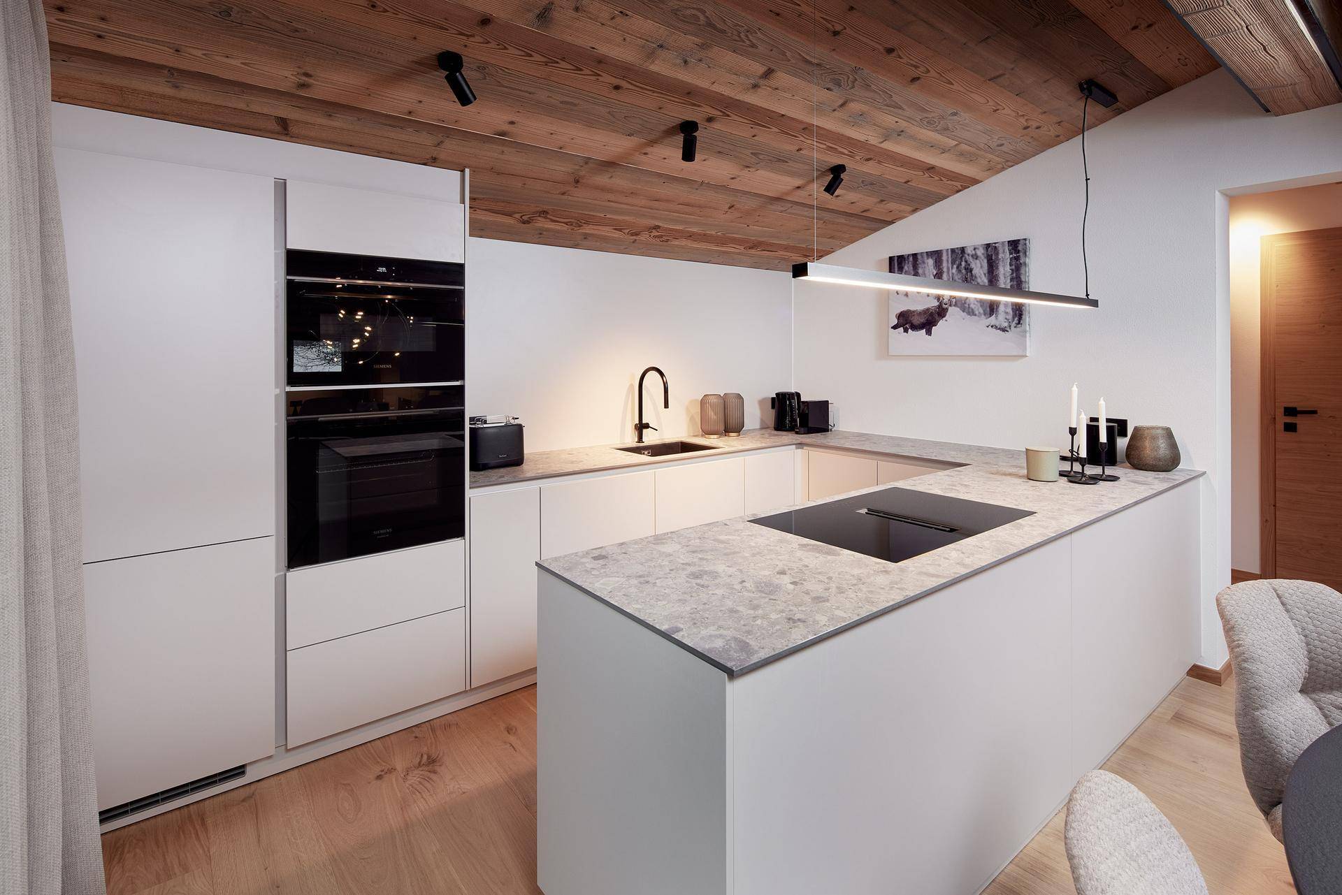 Moderne weiße Küche mit integrierten Geräten, Induktionskochfeld und Stein-Arbeitsplatte.