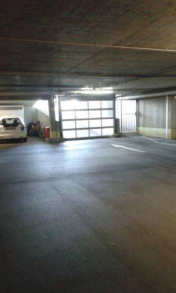 Einfahrt zu einer Tiefgarage mit Rolltor, Fahrrädern und Betonwänden.