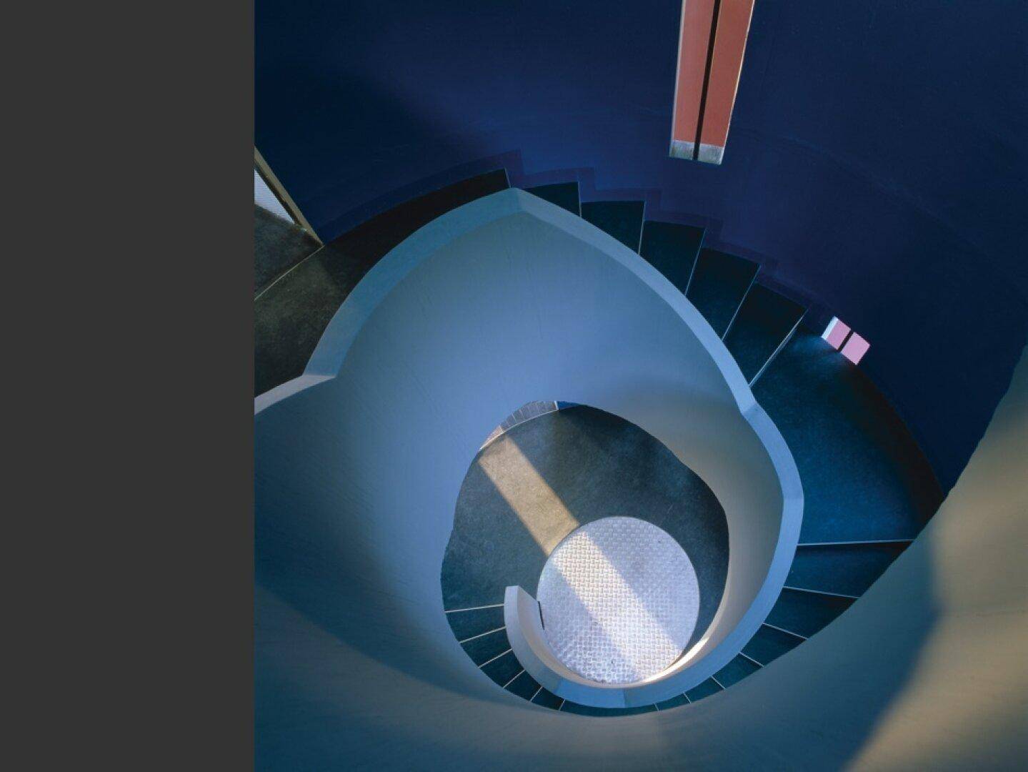 Blick von oben in ein modernes, spiralförmiges Treppenhaus mit blauen Wänden und interessanten Lichteffekten.