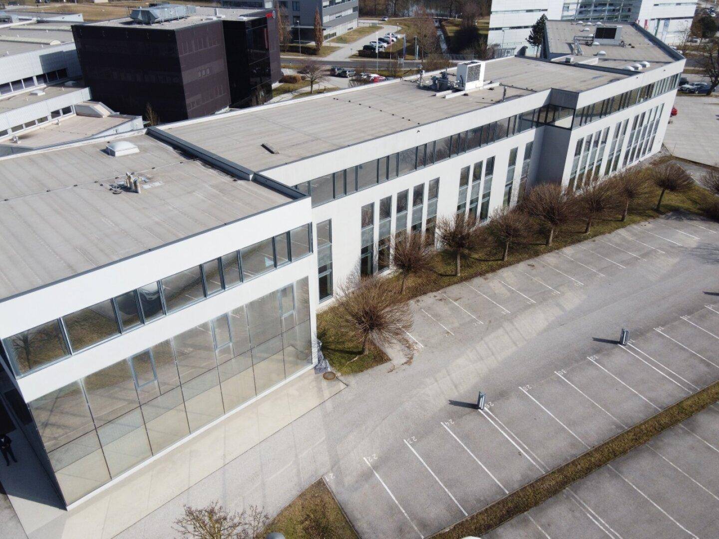 Weitläufige Luftaufnahme des modernen Bürokomplexes mit Parkplätzen und umliegenden Gebäuden unter blauem Himmel.