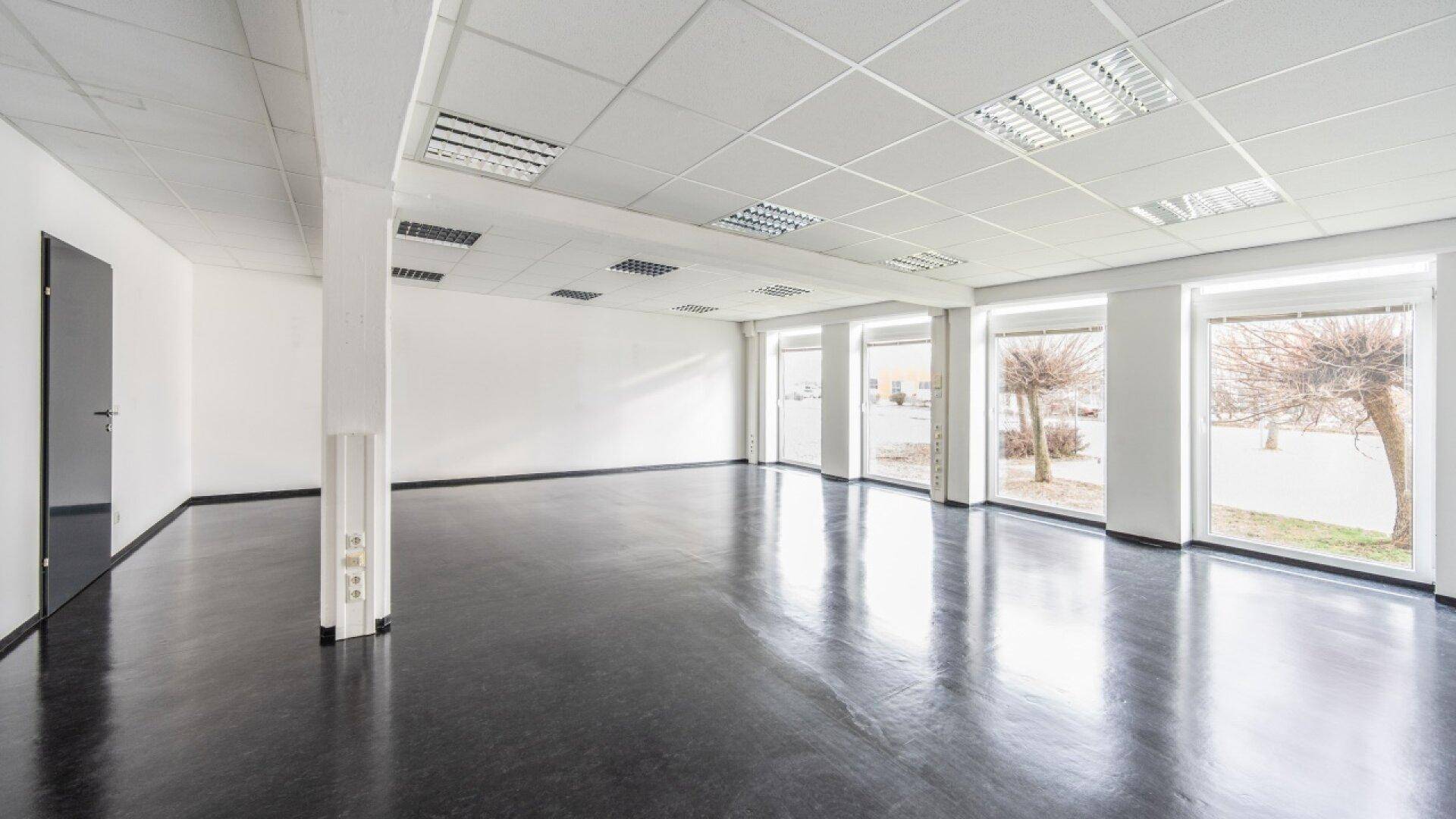 Heller, unmöblierter Bürobereich mit vielen Fenstern, die Tageslicht hereinlassen, und dunklem Bodenbelag.