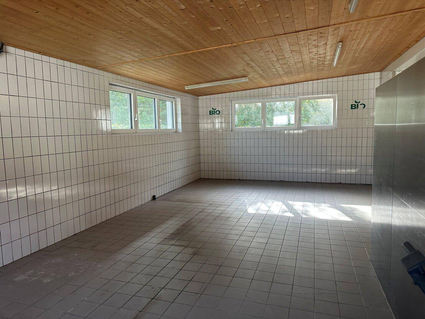 Helle Gewerbeküche mit weißen Fliesenwänden, Holzdecke und Fenstern, die das BIO-Logo tragen.