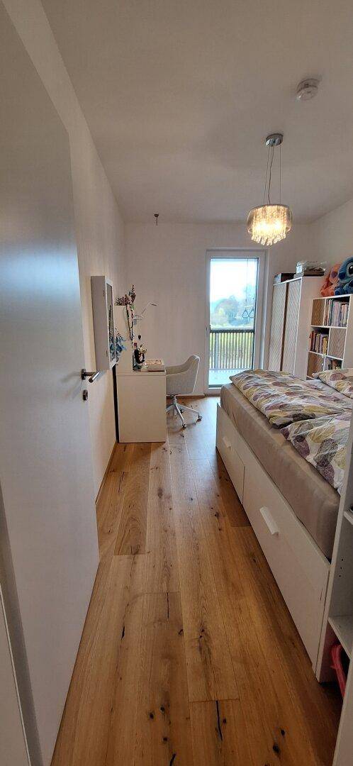 Helles Schlafzimmer mit Holzboden, Bett und Schreibtisch, mit Zugang zu einem Balkon.