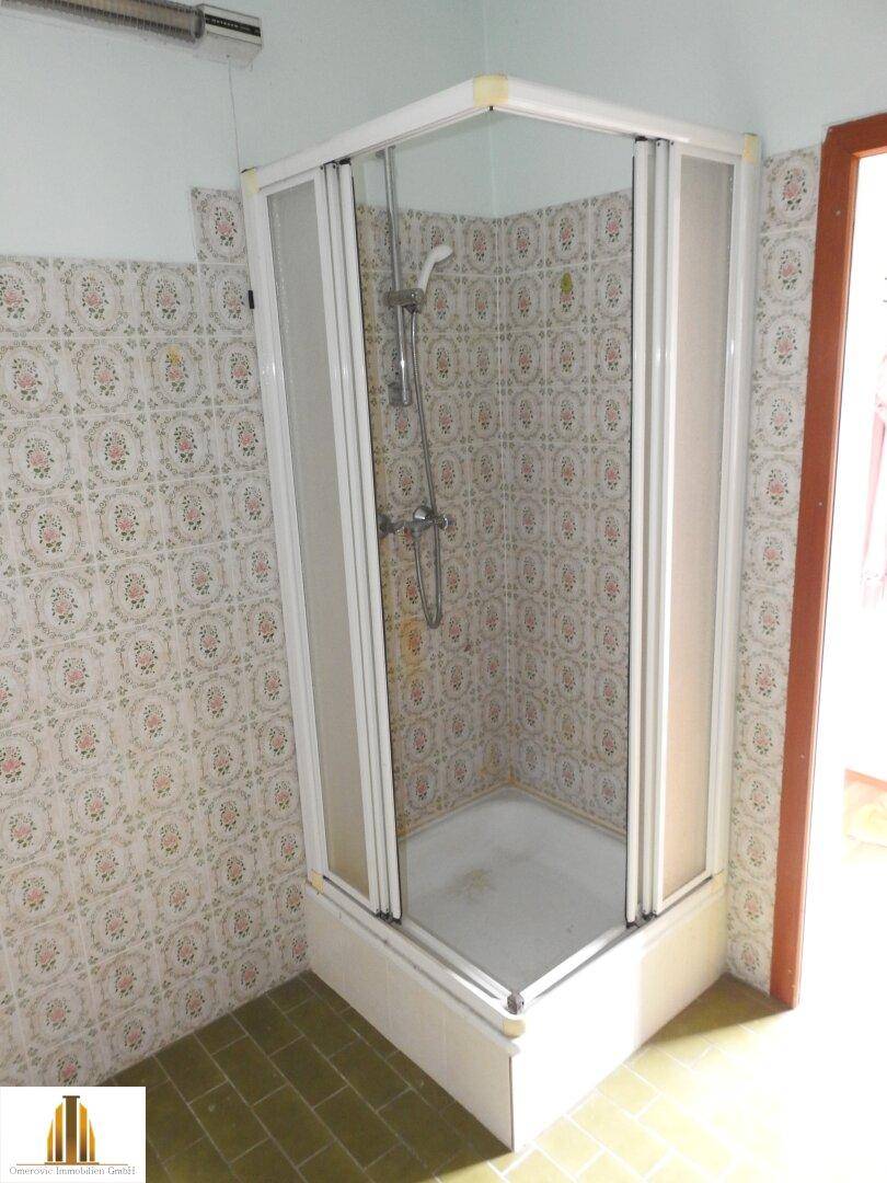 Badezimmer mit einer Duschkabine und den charakteristischen gemusterten Fliesen der 80er Jahre.