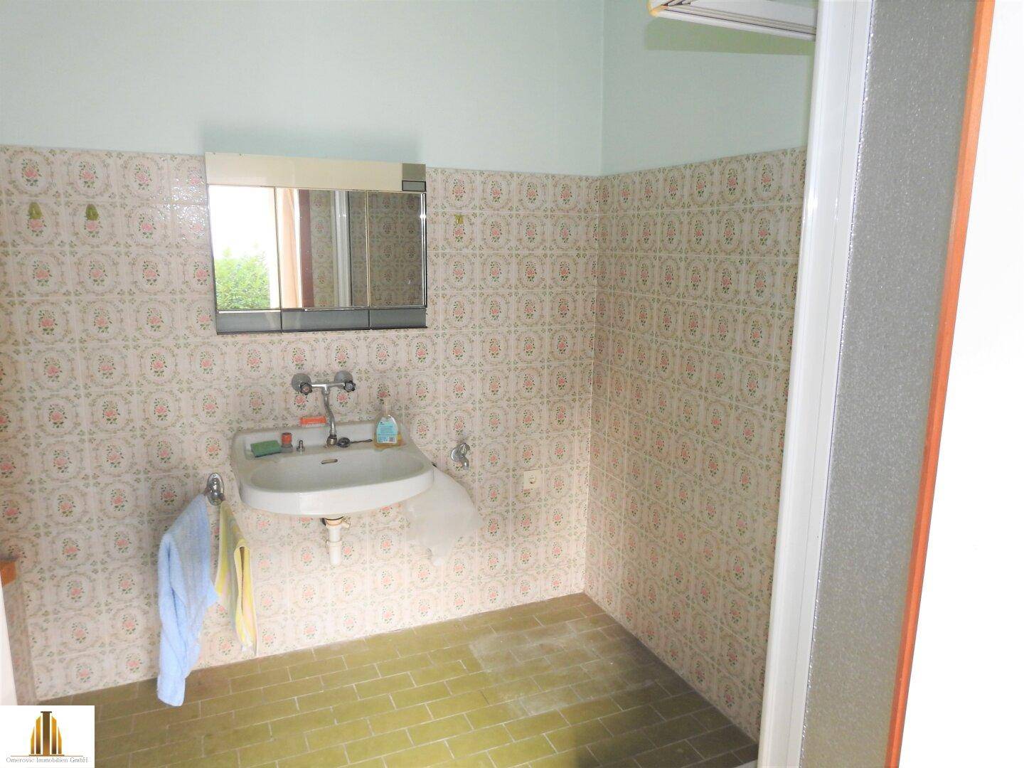 Badezimmer mit Waschbecken, Spiegelschrank und gemusterten Fliesen im Retro-Stil.
