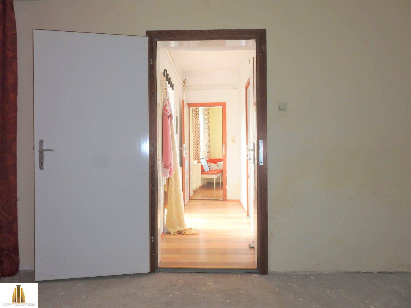 Blick durch eine offene Tür in einen hellen Flur, der zu einem weiteren Zimmer führt.