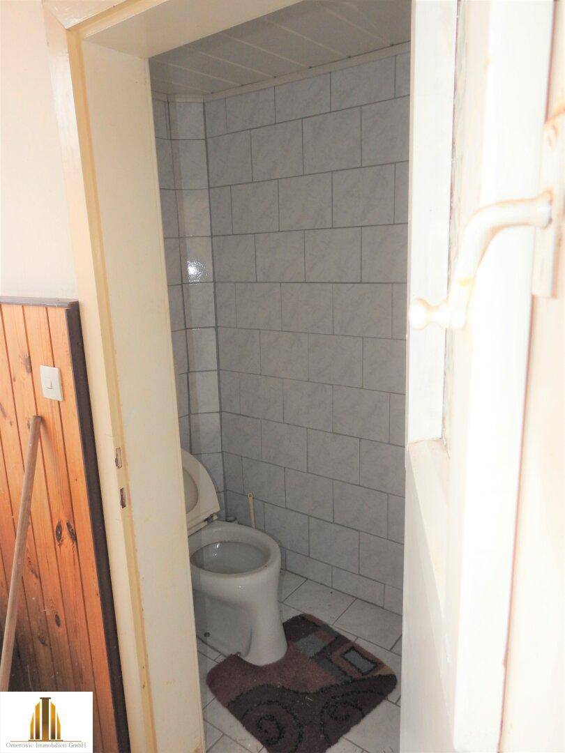 Separate Toilette mit weißen Fliesen an den Wänden und einem kleinen Teppich auf dem Boden.