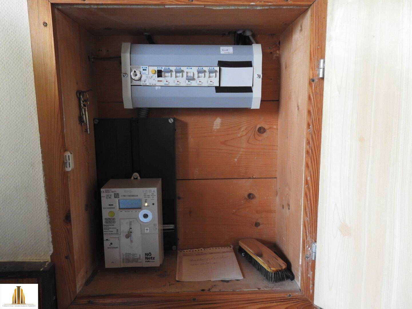 Hauswirtschaftsraum mit sichtbarem Sicherungskasten und Stromzähler in einer Holzverkleidung.