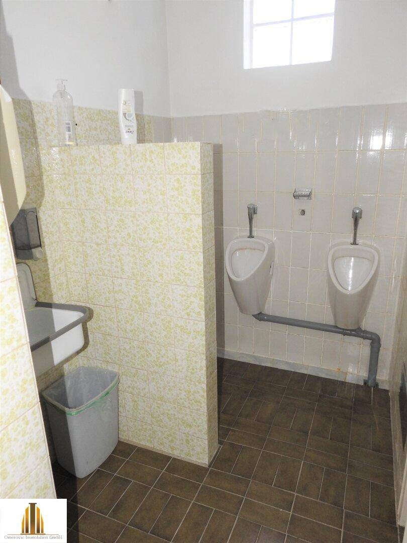 WC-Bereich mit zwei Urinalen und hellgrünen Fliesen, getrennt durch eine Trennwand.