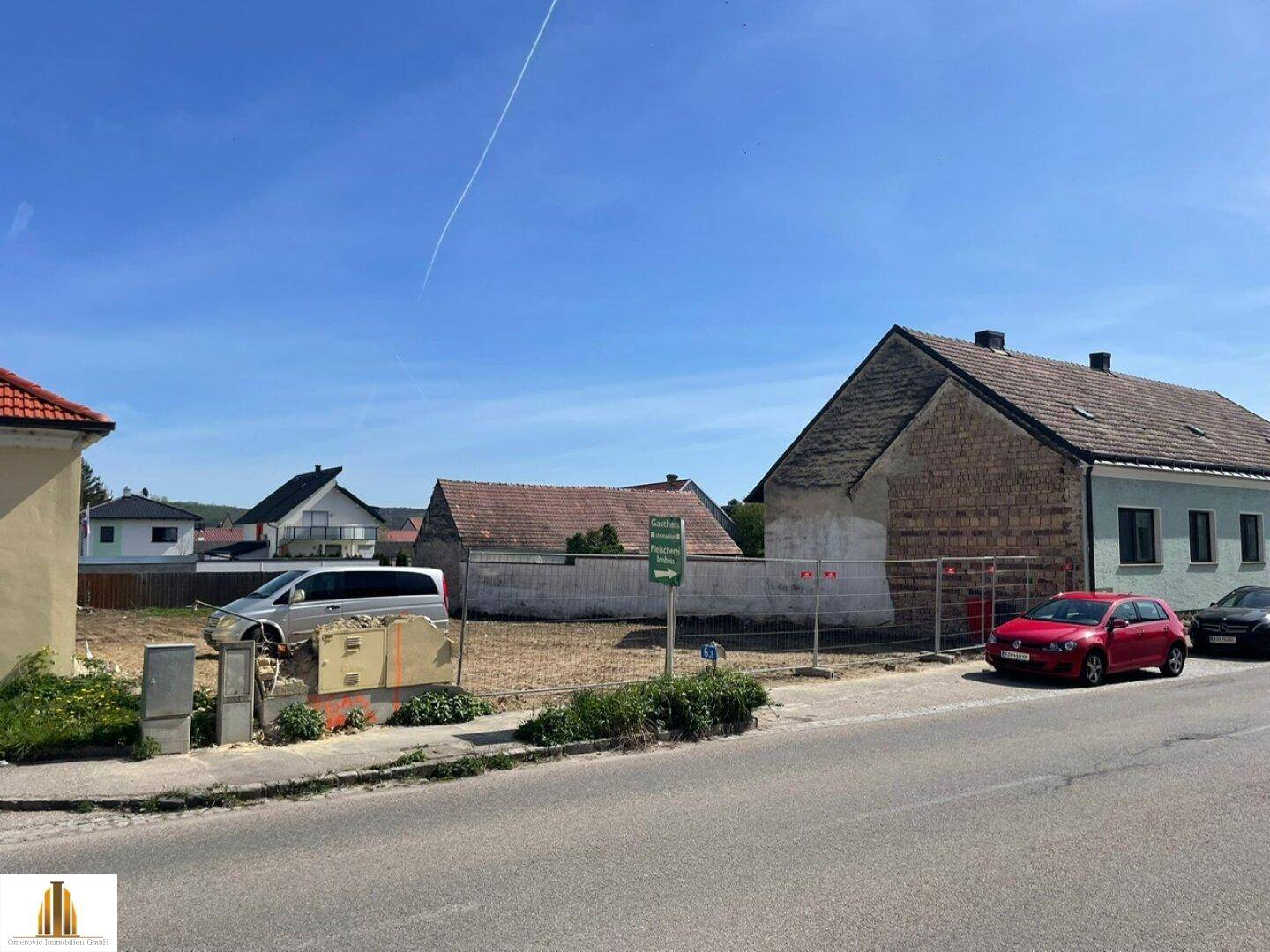 Blick von der Straße auf das freie Grundstück mit angrenzenden Häusern und parkenden Autos.