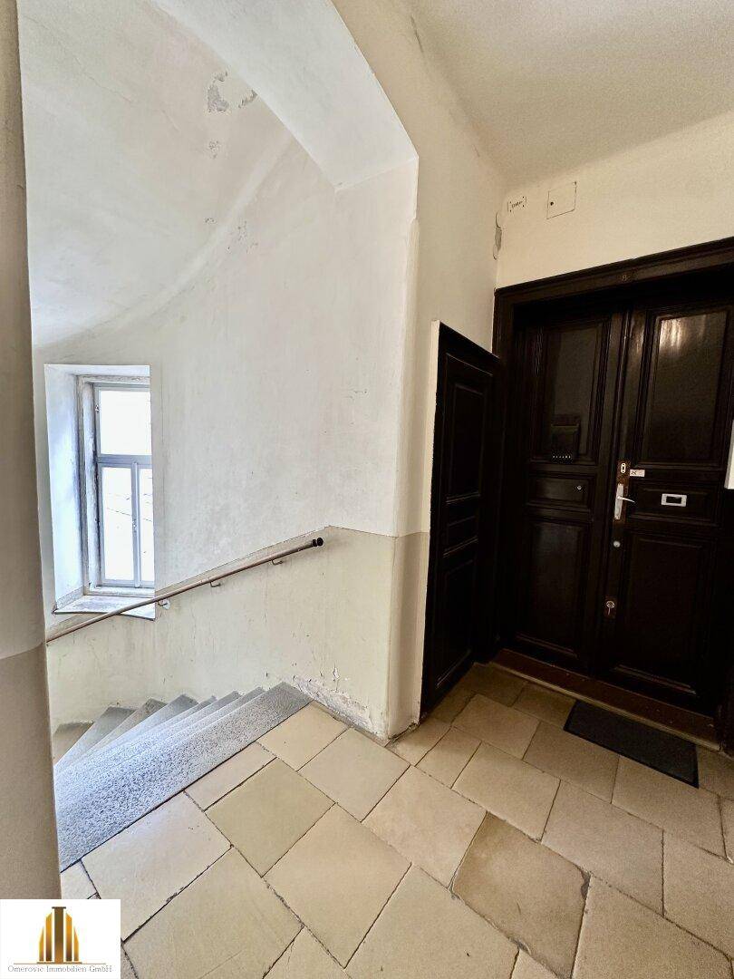 Treppenhaus mit Steinfliesen und dunkler Eingangstür, typisch für ein Altbaugebäude mit historischem Charme.