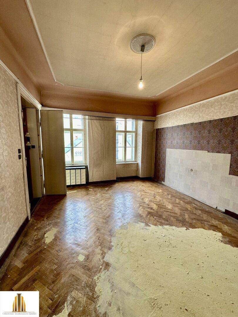Helles Zimmer mit Fischgrätparkett und Stuckdecke, das auf eine Modernisierung wartet.