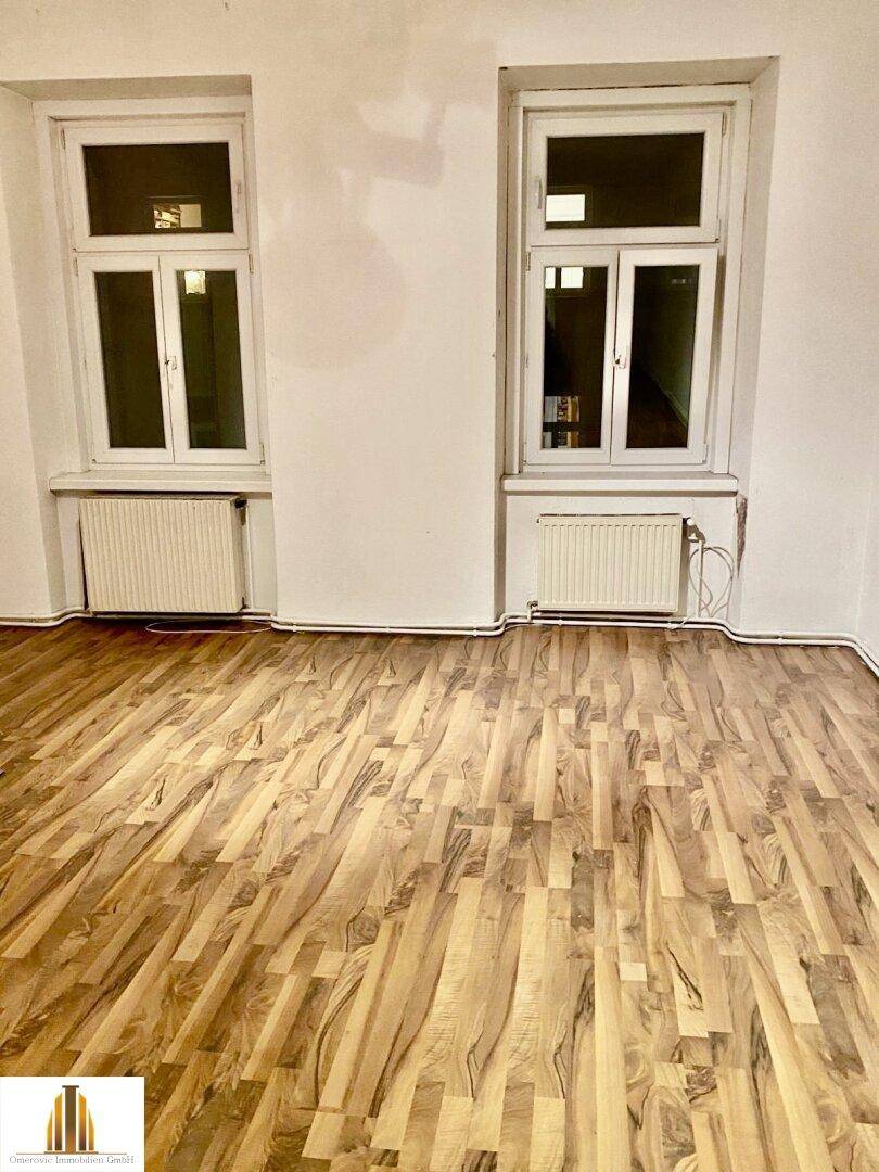 Heller Raum mit Laminatboden und zwei Fenstern, bereit zur individuellen Gestaltung und Nutzung.