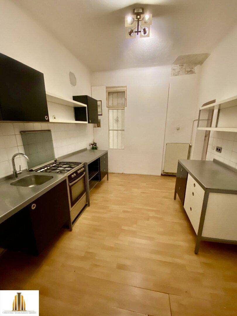Einfache Küche mit Holzfußboden, Gasherd und dunklen Schränken, bietet Potenzial zur Modernisierung.