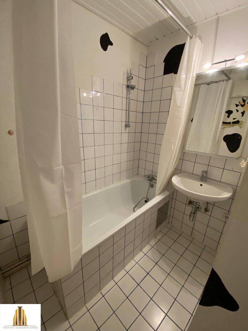 Gefliestes Badezimmer mit Badewanne, Duschvorhang und Waschbecken, in schlichtem und funktionalem Design.