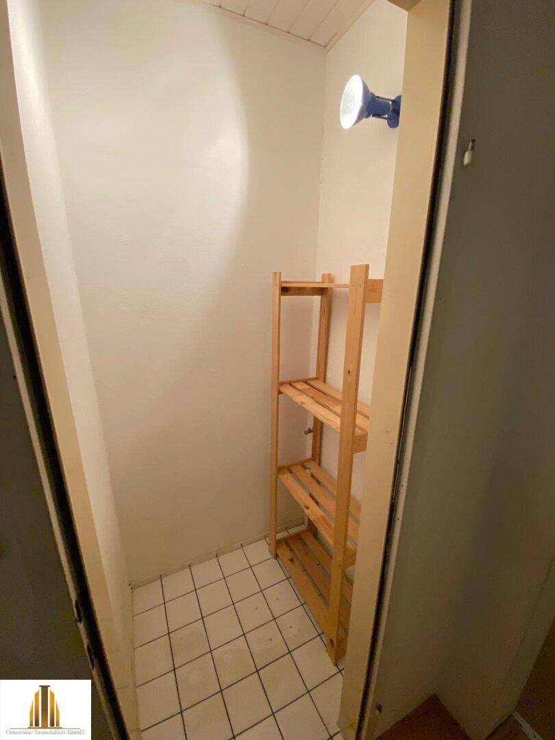 Praktischer Abstellraum mit Fliesenboden und Holzregalen, bietet zusätzlichen Stauraum für Haushaltsgegenstände.