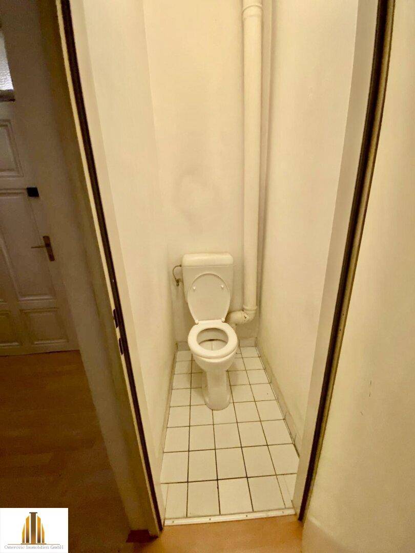Kleines separates WC mit weißer Toilette und Fliesenboden, funktional und einfach gehalten.