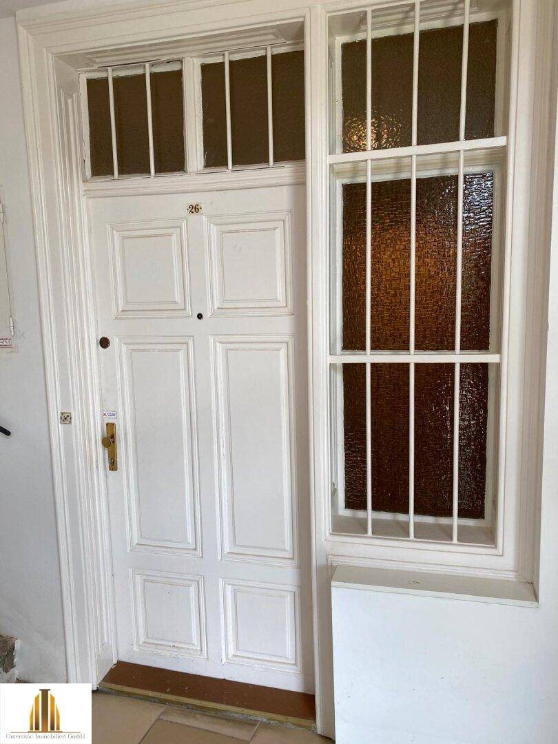 Weiße Eingangstür mit dekorativen Gittern und Oberlicht, führt in die Wohnung und lässt Licht herein.