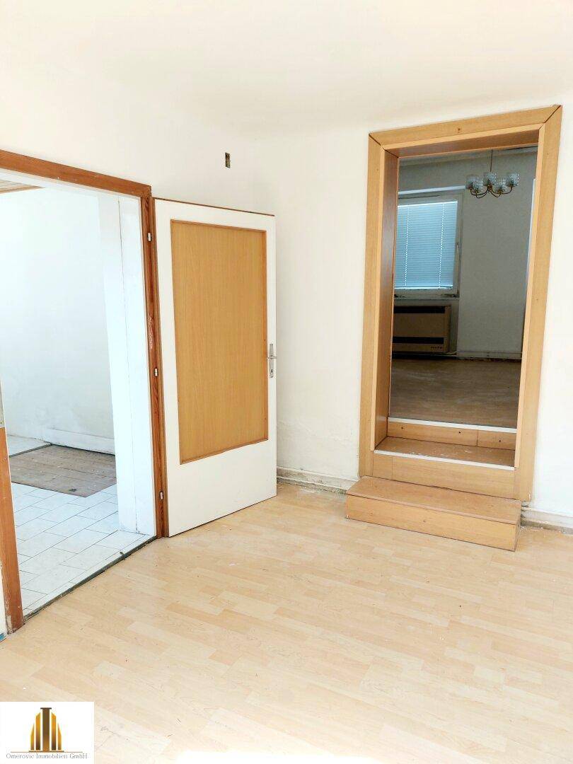 Übergangsbereich mit hellem Parkettboden und einem erhöhten Durchgang zu einem angrenzenden Zimmer.