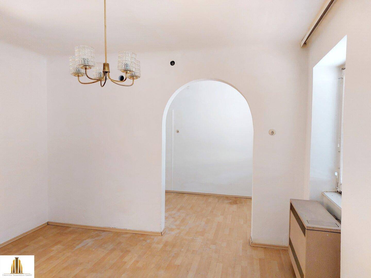 Geräumiges Wohnzimmer mit Parkettboden und einem eleganten Bogen, der zu einem weiteren Raum führt.