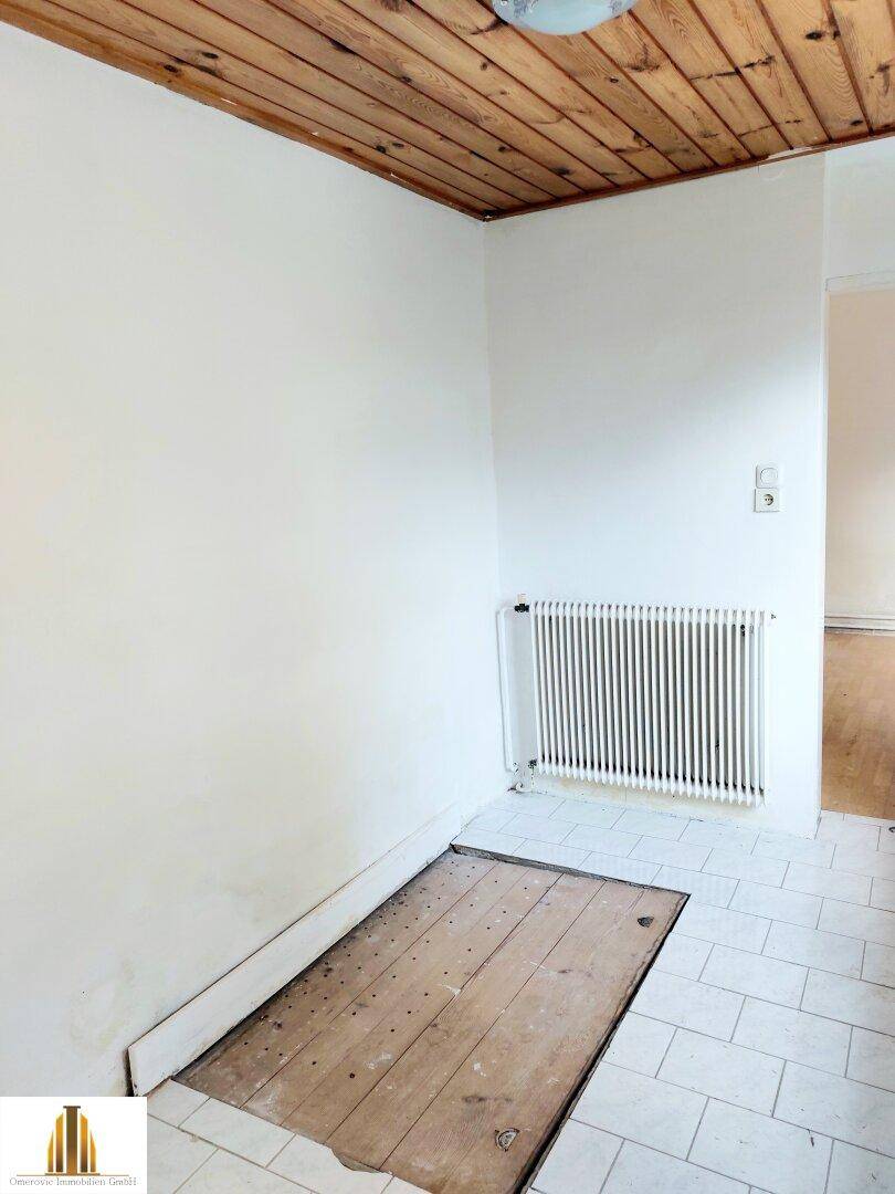 Kleiner Bereich mit Fliesenboden, Holzdecke und Heizkörper, der auf Renovierungsbedarf hindeutet.